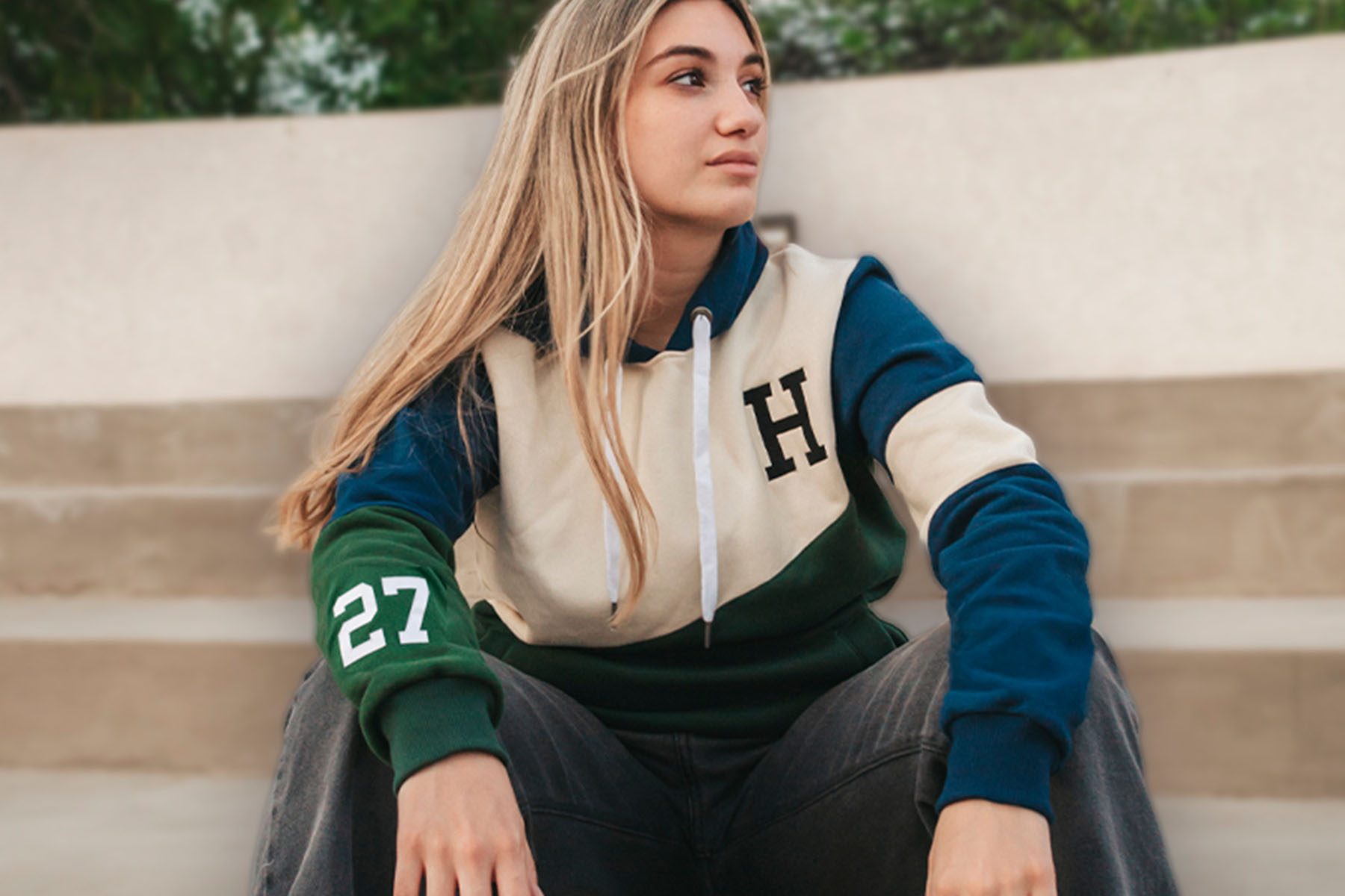 Chica sentada en unas gradas con un buzo de egresados en crema, azul y verde, con la inicial del colegio y el año de la promoción.